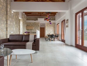 Relax in this stylish living area with a sofa, dining table, and kitchen, surrounded by stone walls and wooden beams.