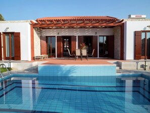 Relax by the rectangular pool surrounded by a stone deck and seating area under a pergola.