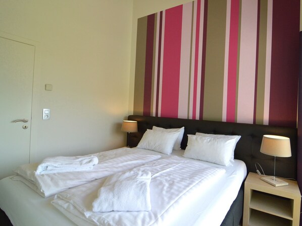A hotel room with a bed, two bedside lamps, a nightstand, and a striped wall.