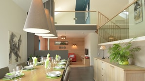 A modern dining area with a long wooden table set for a meal, a staircase leading to an upper level, and a potted plant on a wooden cabinet. - Malmedy Hillside Spa Retreat (Malmedy)