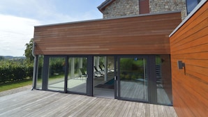 A modern house with a wooden deck, large glass doors, and a stone facade. - Malmedy Hillside Spa Retreat (Malmedy)