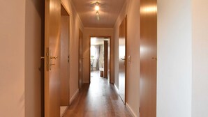 A hallway with wooden floors and doors, leading to a room with a window and curtains.