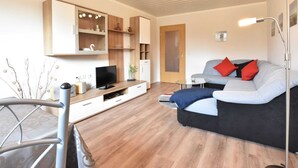 A modern living room with a sofa, TV, wooden shelves, and a door.