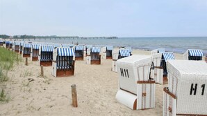 Beach huts with striped awnings, arranged in rows on the sand, near the water.