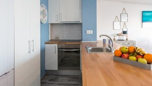 Una cocina compacta con armarios blancos, encimera de madera y frutero.
