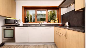 Una cocina moderna con armarios blancos, microondas, horno, pileta y ventana con vista a follaje.