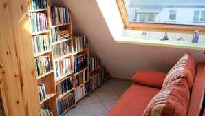 Un rincón acogedor para leer con una estantería de madera llena de libros, un sofá rojo y una mesita con figuritas.