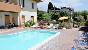 A swimming pool with lounge chairs and umbrellas, surrounded by a brick patio and greenery. - Holiday Home in Lazise Near Lake Garda (Lazise)