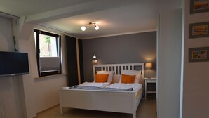 A bedroom with a bed, bedside table, lamp, and a TV mounted on the wall. - Apartment in Robertsdorf Near the Beach (Blowatz)