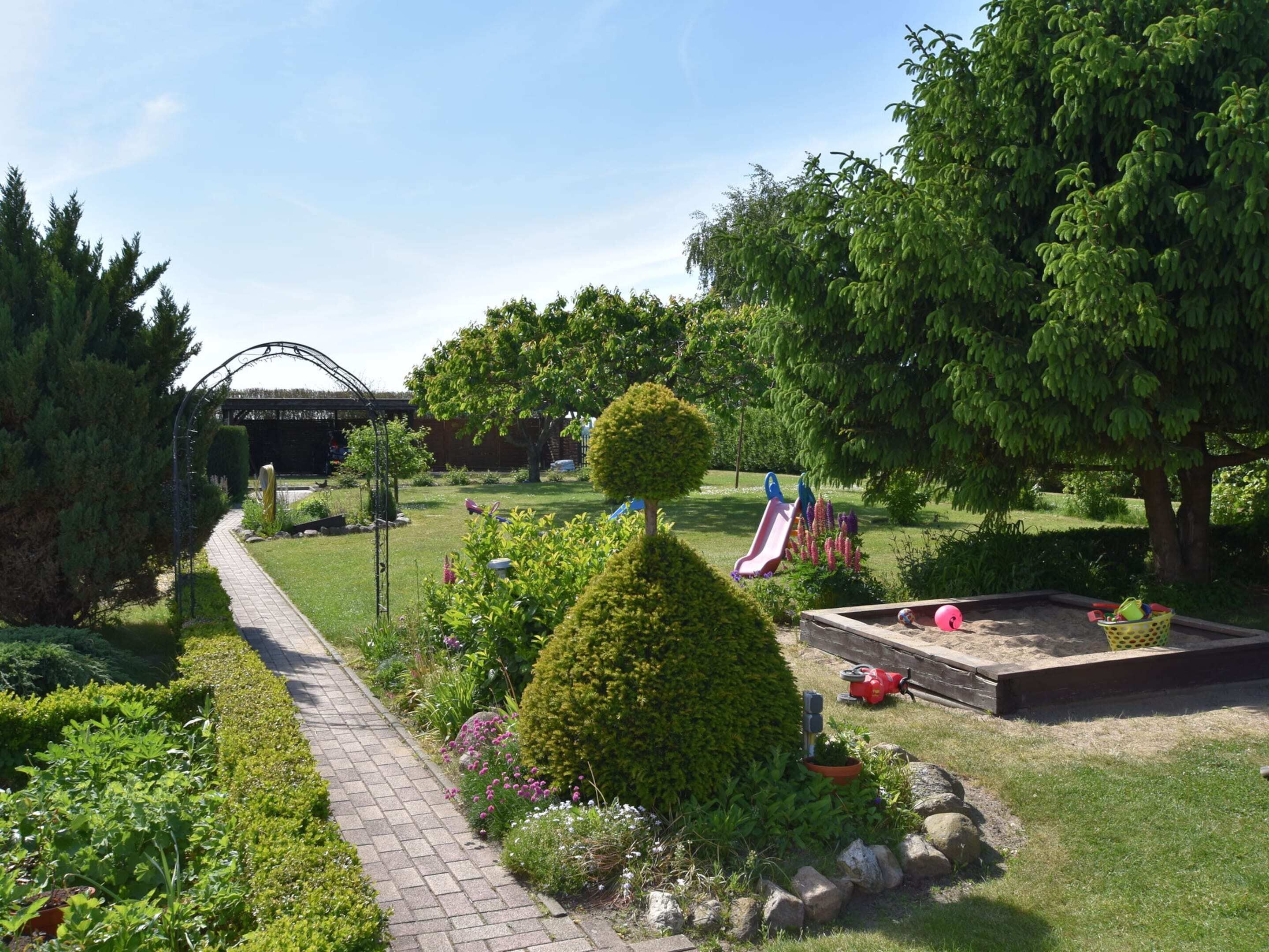 A garden with a paved walkway, a small pond, and a playground with slides.