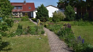 A residential area with a paved pathway, a garden with various plants, and a house with a red roof. - Apartment in Robertsdorf Near the Beach (Blowatz)