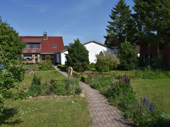 A residential area with a paved pathway, a garden with various plants, and a house with a red roof.