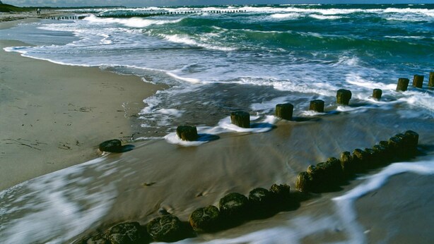 A beach with waves crashing onto the shore, a wooden breakwater, and a clear blue sky. - Apartment in Robertsdorf Near the Beach (Blowatz)