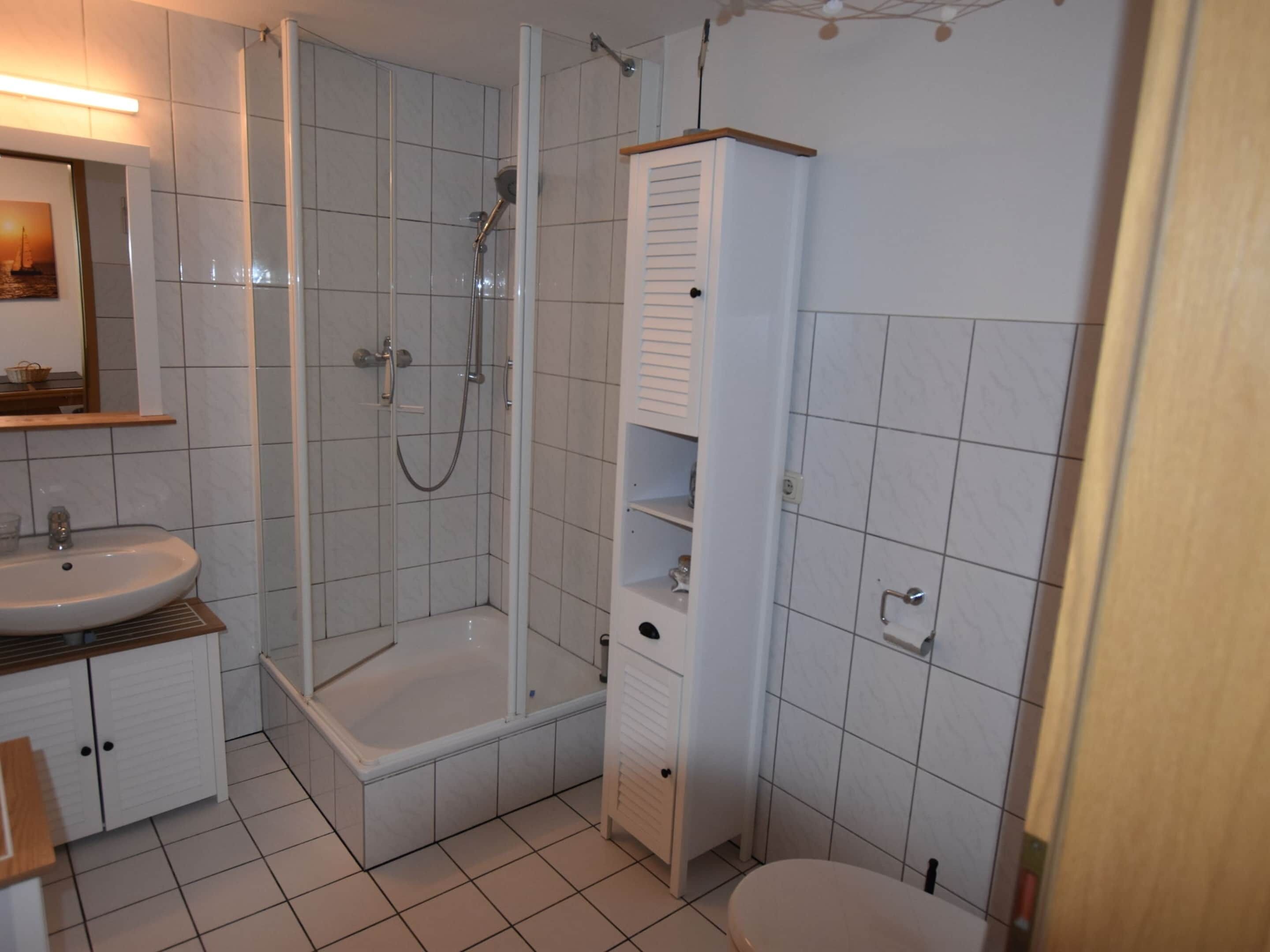 Een badkamer met douche, wastafel, toilet en een hoge kast.