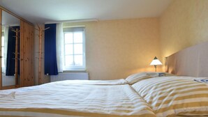 A bedroom with two beds, a window with curtains, a lamp, and a wardrobe.