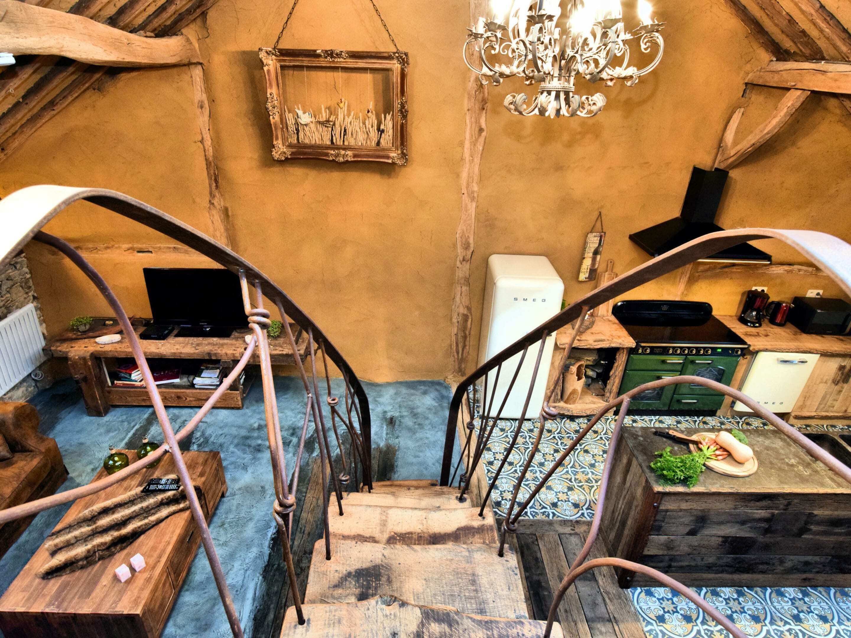A rustic interior with a wooden staircase, a chandelier, a framed picture, and a vintage refrigerator.