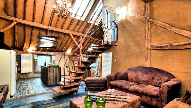 A rustic interior with exposed wooden beams, a spiral staircase, a plush brown sofa, and a wooden coffee table with bottles. - Farmhouse in Durbuy With Sauna & Garden (Durbuy)