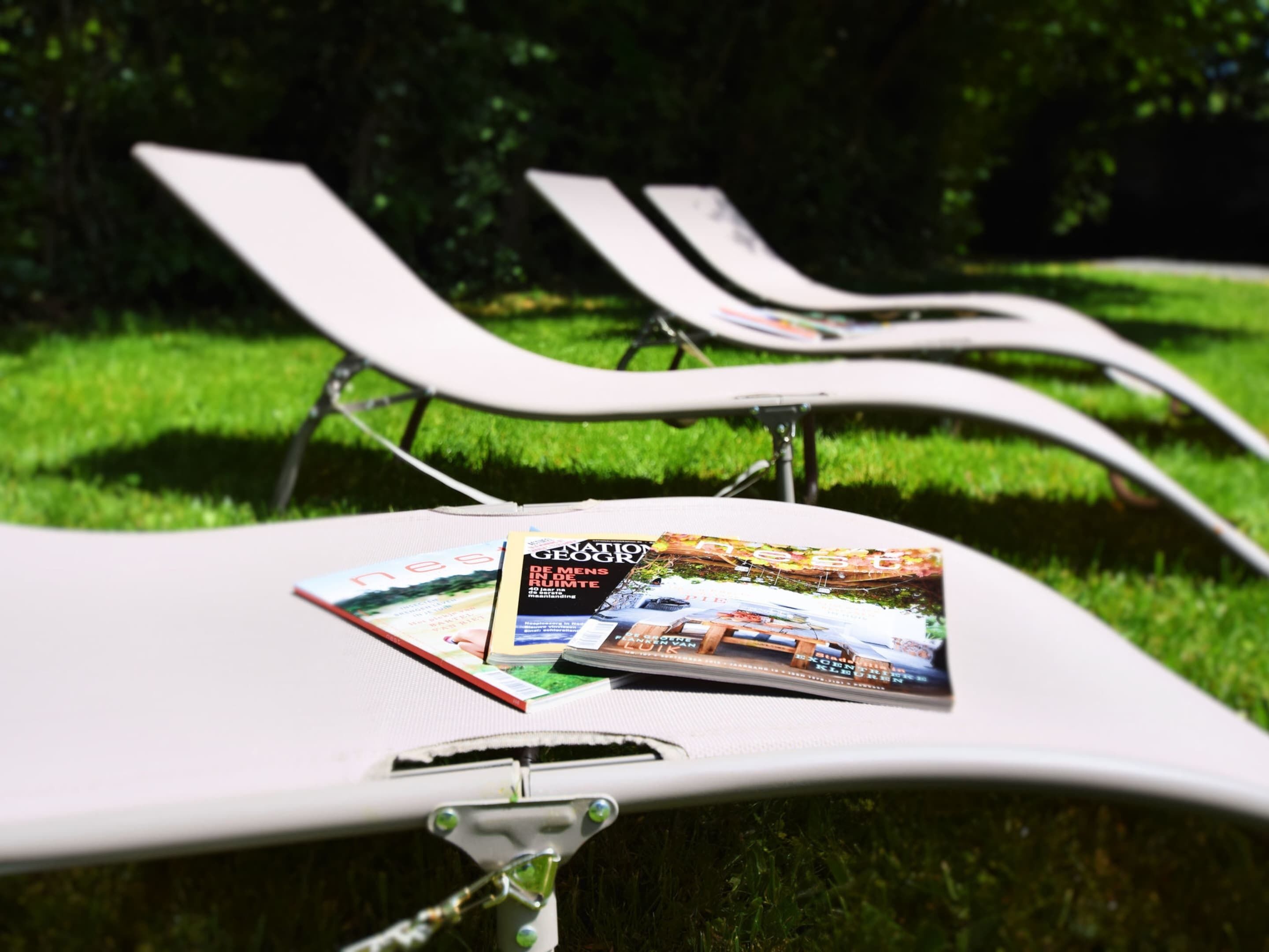 A lounge chair with a magazine on it, set on a grassy area with other lounge chairs in the background.