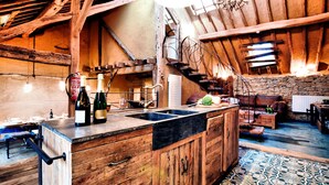 A rustic kitchen with wooden cabinets, a large island, and a stone wall. - Farmhouse in Durbuy With Sauna & Garden (Durbuy)