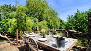 An outdoor dining area with a rustic wooden table and wicker chairs, surrounded by lush greenery and trees. - Farmhouse in Durbuy With Sauna & Garden (Durbuy)