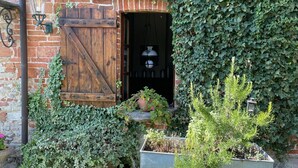 A rustic entrance with a wooden door and a brick wall, surrounded by lush greenery and potted plants. - Holiday Home in Langhe With Pool and Terrace (Bastia Mondovì)