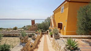 A yellow building with a stone pathway leading to a staircase, overlooking a body of water.