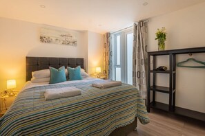 A neatly made bed with striped bedding, a bedside table with a lamp, a painting on the wall, and a window with curtains. - Second Nest Ramsgate flat 1 (Ramsgate)