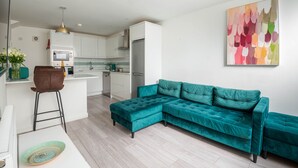 A modern kitchen with white cabinets, a teal sofa, and a bar area.