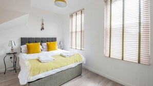 Ein Schlafzimmer mit einem Bett, Nachttischlampen, einem hängenden Traumfänger und einem Fenster mit Jalousien.