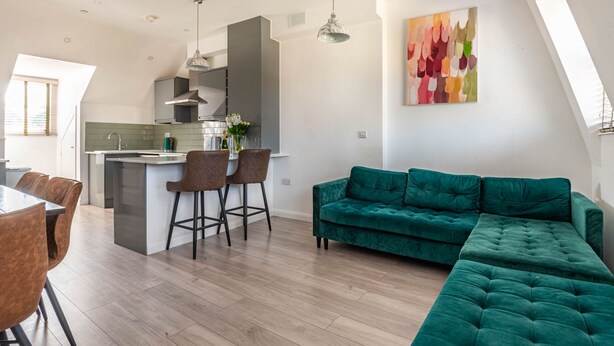 Eine moderne Küche mit einer zentralen Kochinsel, Barhocker und einem grünen Sofa.