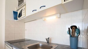Een keuken met een roestvrijstalen spoelbak, witte kastjes en een blauwe houder voor keukengerei.