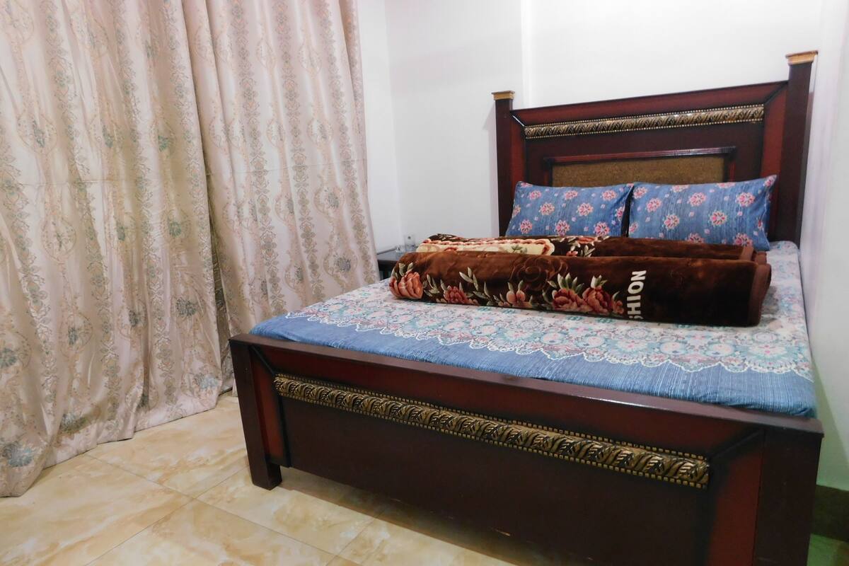 A bed with a floral bedspread and a brown blanket, a wooden headboard, and a blue pillow with a floral pattern.