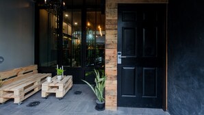 Un banco de madera, una mesita con una planta en maceta y una puerta negra.