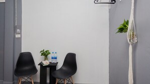 A room with two black chairs, a small table with a plant and water bottles, a macrame wall hanging, and a white hanger on the wall. - Boho Bangkok (Bangkok)