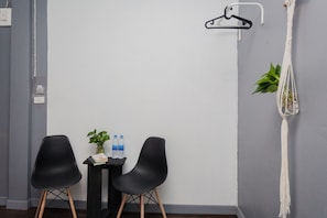 A room with two black chairs, a small table with a plant and water bottles, a macrame wall hanging, and a white hanger on the wall. - Boho Bangkok (Bangkok)
