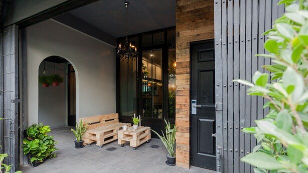 An outdoor seating area with a wooden bench and tables, surrounded by potted plants and a black door. - Boho Bangkok (Bangkok)