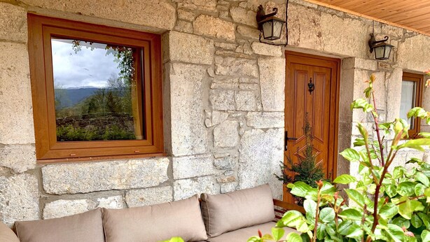 Ein Steinhaus mit einer Holztür und einem Fenster, einem beigen Sofa und einer Topfpflanze.
