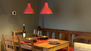 Ein Essbereich mit einem Holztisch, zwei roten Pendelleuchten, einer Weinflasche und zwei Gläsern.