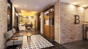 Un hall de hotel con suelo a cuadros, una zona de estar con sofás y una mesa de centro, y una gran 'B' en la pared de ladrillo.