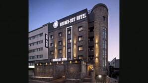 Un hotel moderno con un letrero destacado que dice "BROWN-DOT HOTEL". Cuenta con fachada de ladrillo, varias ventanas y una estructura en esquina curva.