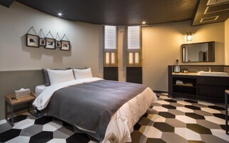 Un dormitorio moderno con una cama grande, una mesita de noche, un tocador, un baño con lavamanos y espejo, y un suelo con estampado geométrico.