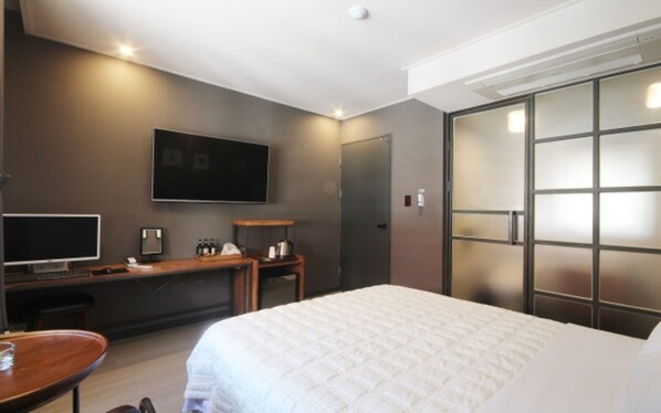 Habitación de hotel con cama, escritorio con computadora, televisión y armario con puertas de vidrio esmerilado.