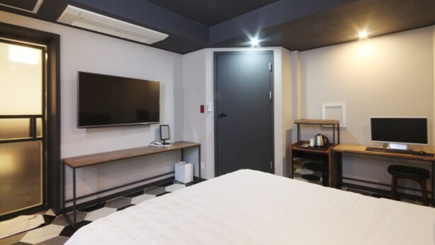 Una habitación de hotel con una cama, un escritorio con computadora, un televisor y una puerta.