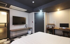 Una habitación de hotel con una cama, un escritorio con computadora, un televisor y una puerta.