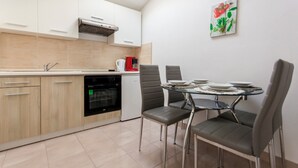 A modern kitchen with white cabinets, a built-in oven, and a dining area with a glass table and four chairs. - Adorable House Apartment With Roof Terrace (Malinska-Dubasnica)