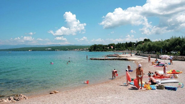 A beach with clear turquoise water, people sunbathing, and a dock extending into the sea. - Adorable House Apartment With Roof Terrace (Malinska-Dubasnica)