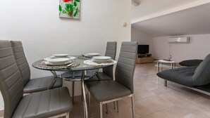 A modern living room with a dining area. It includes a round glass table with four chairs, a sofa, a flat-screen TV, and a small side table. - Adorable House Apartment With Roof Terrace (Malinska-Dubasnica)