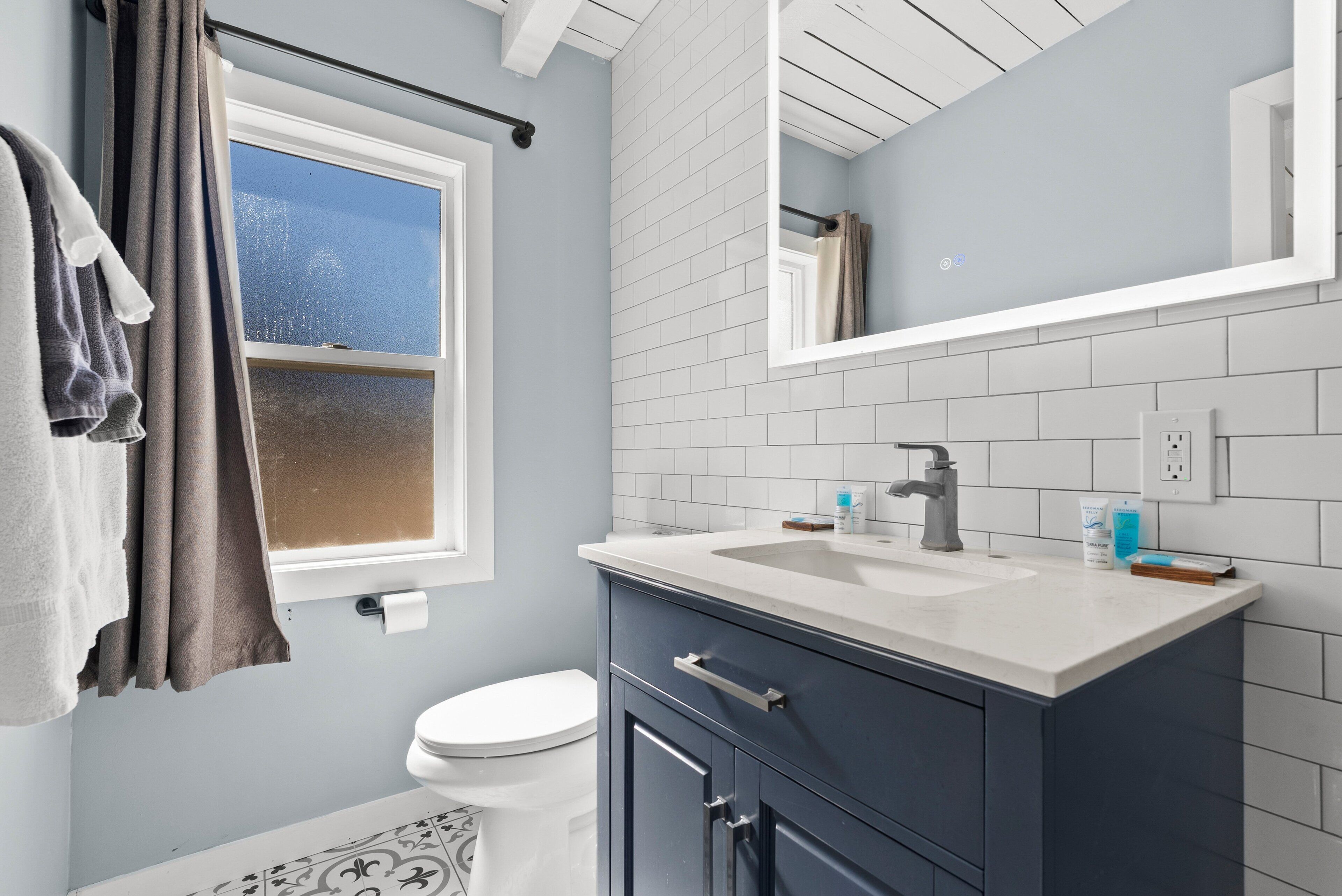 A bathroom with a toilet, a sink, a mirror, and a window.