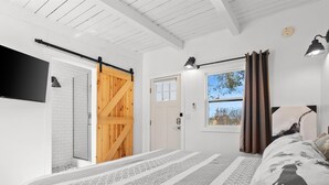 A bedroom with a bed, a window with curtains, a door, and a mounted TV. - WWM 3 · 3 Explore, Swim, Dream, The E Sierras WWM 3 (Coleville)