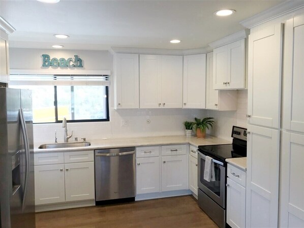 A modern kitchen with white cabinetry, stainless steel appliances, and a window with a view.